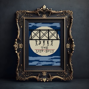 May include: A framed cross-stitch design featuring a silhouette of five figures walking across a bridge under a full moon. The text "THE LOST BOYS" is below the bridge.