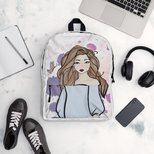 May include: White backpack featuring an illustration of a woman with long brown hair and a light blue top. The design includes watercolor-style splashes of purple and pink, and a butterfly. The backpack has a black handle and zipper.