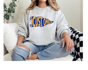 May include: A light gray sweatshirt with the word "CUSTOMIZE" in a blue and yellow pennant design. The sweatshirt is long-sleeved and has a crew neck. The person in the image is wearing blue jeans.