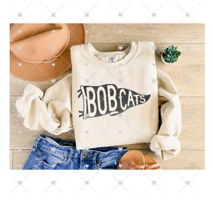 May include: A cream-colored sweatshirt with a black pennant design that says "BOBCATS" on a wood background.