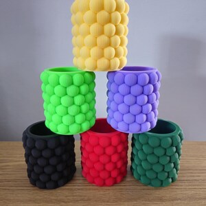 May include: Six colourful cylindrical containers with a textured bubble design. The containers are stacked in a pyramid shape, with the yellow container at the top and the green container at the bottom.