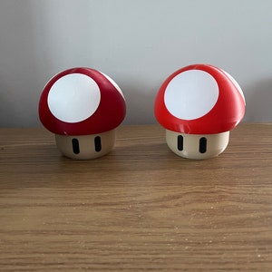 May include: Two red and white mushroom-shaped figurines with black eyes.