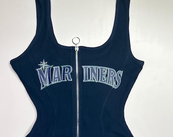 May include: Navy blue tank top with a silver zipper and the text "MARINERS" in white and blue. The top has a fitted silhouette and a scoop neckline. The tank top is made of a ribbed material.