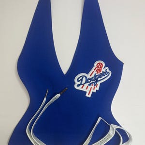 Può includere: Top all'americana blu reale con il logo dei Los Angeles Dodgers ricamato sul davanti. Il top presenta uno scollo a V e spalline bianche con strass. Il top è realizzato in tessuto a maglia a coste.