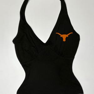 May include: A black halter top with a V-neckline and a fitted silhouette. An orange Longhorn logo is on the chest. The top has a smooth texture and a classic design.