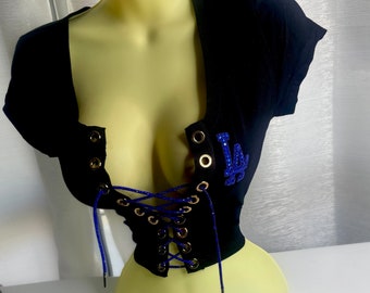 May include: Black crop top with a blue and white "LA" rhinestone design. The top features a lace-up front with gold grommets.