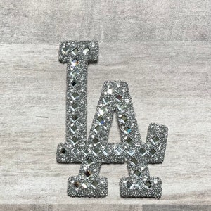 Può includere: Una toppa LA in glitter argento con strass a specchio.