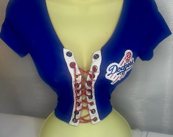 May include: Blue and white cropped t-shirt with a red and white lace-up front and a "Dodgers" logo patch on the right side.