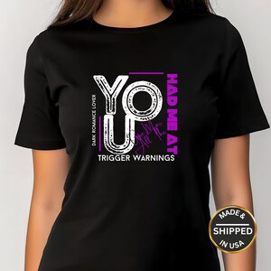 May include: Black t-shirt with a white and purple graphic design. The design includes the words "YO UP" and "HAD ME AT" with the text "DARK ROMANCE LOVER" and "TRIGGER WARNINGS". The shirt is made and shipped in the USA.