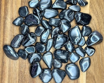 Op de afbeelding: Een verzameling gladde, zwarte hematiet-tumbled stenen. De stenen zijn van verschillende groottes en vormen, met een glanzende, metallic afwerking.