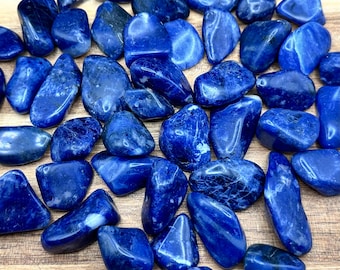 Op de afbeelding: Een verzameling van getrommelde blauwe sodalietstenen. De stenen zijn glad en gepolijst, met een diepblauwe kleur en witte aderen.