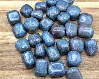 Op de afbeelding: Een verzameling van getrommelde blauwe kyanite stenen met rode insluitsels. De stenen zijn glad en gepolijst, en ze hebben verschillende vormen en maten.