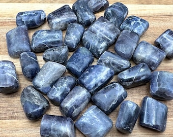 Op de afbeelding: Een verzameling van getrommelde blauwe kyanite stenen. De stenen zijn glad en gepolijst, met verschillende tinten blauw. Ze zijn willekeurig gerangschikt op een houten oppervlak.
