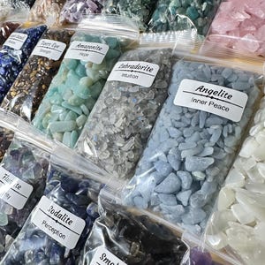 May include: Assortment of small, colorful tumbled gemstones in clear plastic bags. Each bag has a label with the gemstone name and a related word. Gemstones include Tiger's Eye, Amazonite, Labradorite, Angelite, Sodalite, and Smokey Quartz.