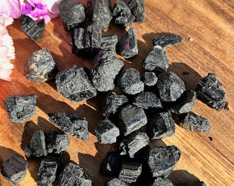 Op de afbeelding: Een verzameling zwarte toermalijnkristallen, ook wel schorl genoemd, op een houten oppervlak. De kristallen zijn ruw en hebben een natuurlijke, onbewerkte uitstraling.