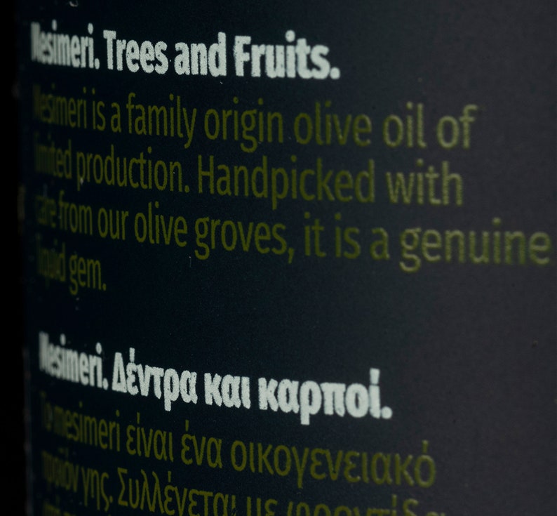 May include: Close-up of a black bottle label with white text that reads "Mesimeri. Trees and Fruits."  The text continues, "Mesimeri is a family origin olive oil of limited production. Handpicked with care from our olive groves, it is a genuine liquid gem."  The label also includes text in Greek.