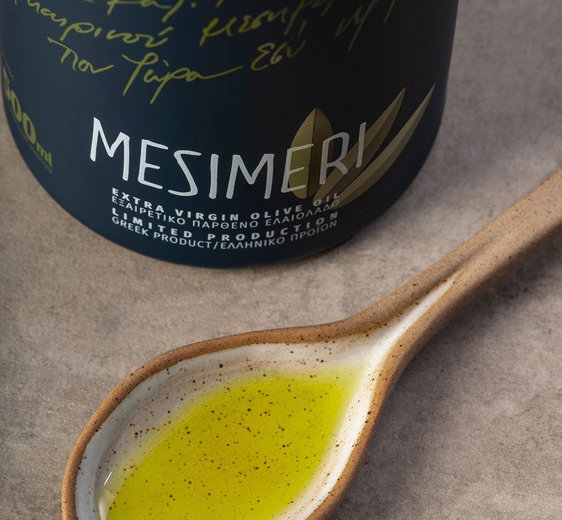 May include: A dark blue bottle of Mesimeri Extra Virgin Olive Oil with a gold leaf design. The bottle is labeled with the text "Mesimeri Extra Virgin Olive Oil", "&Epsilon;&xi;&alpha;&iota;&rho;&epsilon;&tau;&iota;&kappa;ό &Pi;&alpha;&rho;&theta;έ&nu;&omicron; &Epsilon;&lambda;&alpha;&iota;ό&lambda;&alpha;&delta;&omicron;", "Limited Production", and "Greek Product/&Epsilon;&lambda;&lambda;&eta;&nu;&iota;&kappa;ό &Pi;&rho;&omicron;ϊό&nu;".