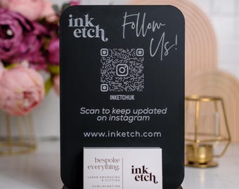 Könnte beinhalten: Ein schwarzes Schild mit weißem Text, der "ink etch" und "Follow Us!" lautet, mit einem QR-Code, der darunter "inketchuk" sagt. Das Schild sagt auch "Scan to keep updated on instagram" und "www.inketch.com". Eine Visitenkarte mit dem Text "bespoke everything" und "ink etch" befindet sich vor dem Schild.