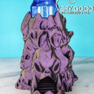 Può includere: Un porta-lattine stampato in 3D di colore viola e nero a forma di mostro con la bocca aperta per contenere una lattina di birra. Il porta-lattine è realizzato da Very Good 3D Printing Co.