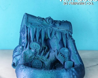 May include: A teal blue 3D printed treasure chest with a monster's mouth open, revealing gold coins inside. The chest is sitting on a white surface.  "VERY GOOD 3D PRINTING CO." is printed on the background.