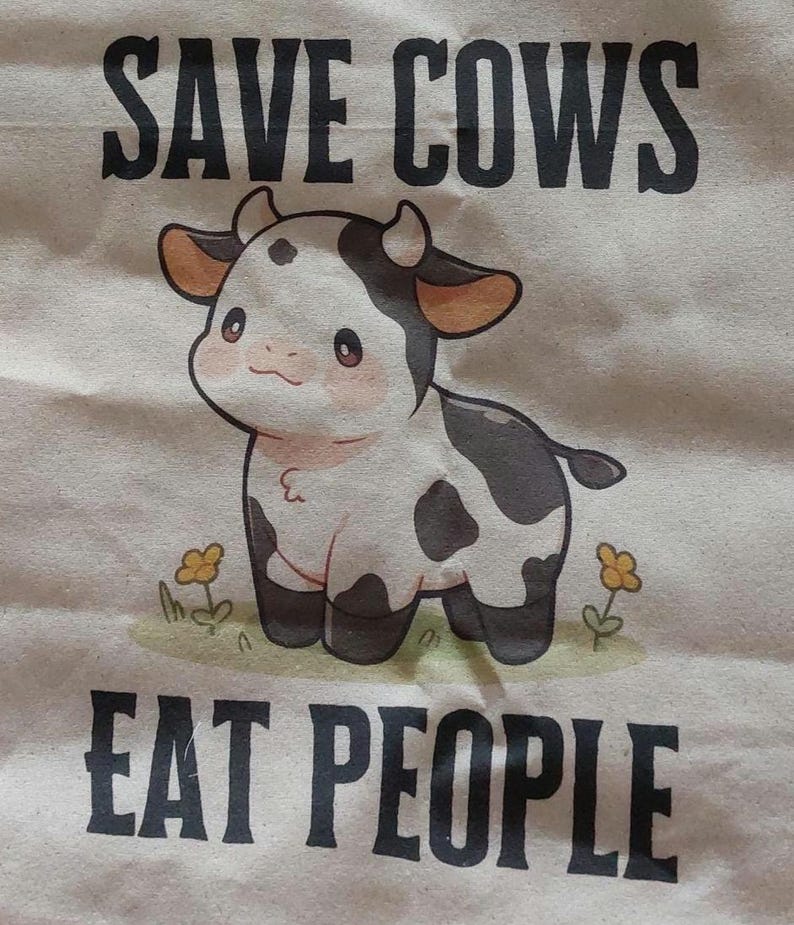 K&ouml;nnte beinhalten: Eine Tragetasche aus Segeltuch mit dem Text "SAVE COWS EAT PEOPLE" in Schwarz. Die Tasche zeigt eine Cartoon-Illustration einer schwarz-wei&szlig;en Kuh mit rosa Rouge und kleinen gelben Blumen.
