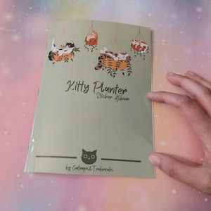Puede incluir: Un álbum de pegatinas verde claro titulado "Kitty Planter" con ilustraciones de gatos en macetas colgantes. La portada presenta el texto "Sticker Album" y el nombre del artista, "by Catnaps & Teabreaks."
