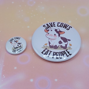 Könnte beinhalten: Zwei weiße runde Buttons mit einer Cartoon-Kuh-Illustration. Der größere Button hat den Text "SAVE COWS EAT PEOPLE". Der kleinere Button hat das gleiche Design und den gleichen Text. Die Kuh ist weiß mit braunen Flecken.