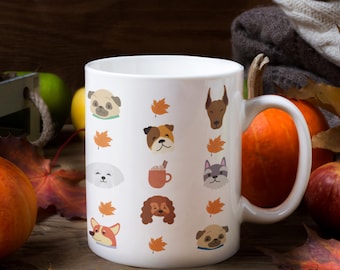 May include: A white ceramic mug featuring a repeating pattern of various dog breeds, including pugs, a bulldog, and a corgi, interspersed with orange autumn maple leaves and a small brown mug of hot cocoa with cinnamon sticks on the front surface.
