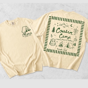 May include: A cream-coloured t-shirt featuring dark green graphics. The front displays a tent icon with the text Olivia Yosemite 2026. The back features a square border enclosing the text Cousin Camp Making Memories Together Yosemite 2026, surrounded by illustrations of mountains, a backpack, a campfire, a tent, and a signpost.