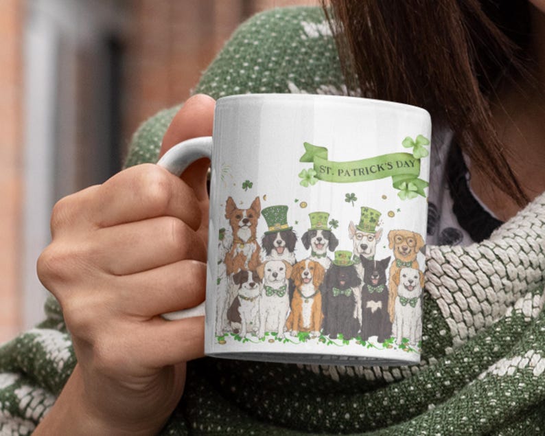 May include: White ceramic mug with a green, white, and gold design featuring a group of dogs wearing St. Patrick's Day hats and a banner that reads "St. Patrick's Day".