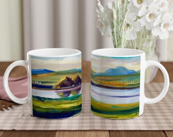 May include: Two white ceramic mugs with a landscape scene painted on them. The mugs have a handle on the right side. The scene on the left mug features a mountain range in the background, a lake in the foreground, and a small island with trees. The scene on the right mug features a mountain range in the background, a lake in the foreground, and a field of grass.