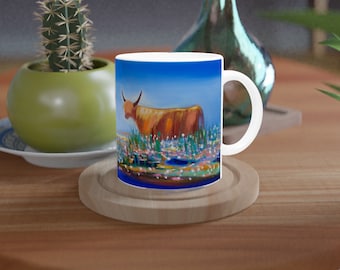 May include: A white ceramic mug featuring a colourful painting of a brown Highland cow standing in a field of flowers. The mug has a blue background and a white handle.
