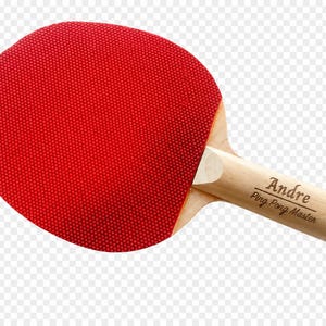 May include: A red ping pong paddle with a wooden handle. The paddle's face is a vibrant red with a textured surface. The handle is light-colored wood, with the name "Andre" and "Ping Pong Master" printed on it.