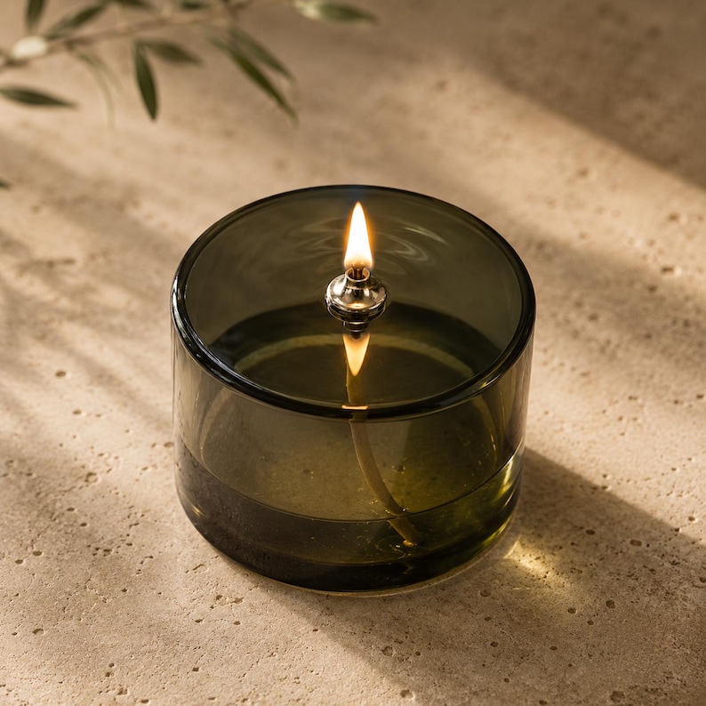 close up of single green glass oil candle with steady flame and transparent glass body