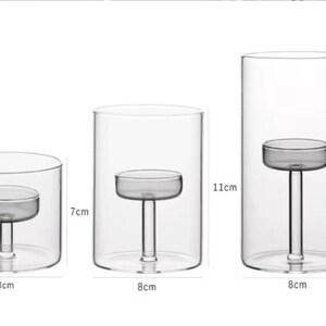May include: Set of three clear glass candle holders. The smallest is 8 cm wide and 7 cm tall, the medium is 8 cm wide and 11 cm tall, and the largest is 8 cm wide and 15 cm tall. Each has a small platform inside to hold a candle.