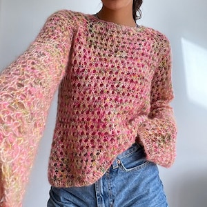 May include: A pink, green and yellow knitted jumper with a loose fit and long sleeves. The jumper has a delicate openwork pattern.