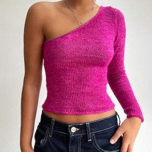 May include: A bright pink one-shoulder sweater with a long sleeve. The sweater is made of a soft, textured knit fabric.