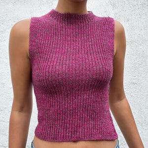 Puede incluir: Un top sin mangas de punto acanalado en color fucsia vibrante con cuello alto. El top tiene un aspecto texturizado y un ajuste ceñido. La tela parece ser una mezcla de hilos fucsia y grises.
