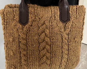 May include: A brown knitted tote bag with leather handles. The bag has a cable knit pattern.