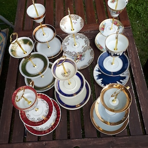 Könnte beinhalten: Ein Set aus zehn zweistöckigen Kuchentellern mit goldenen Griffen und verschiedenen Blumenmustern. Die Teller sind aus weißem Porzellan mit goldenen Akzenten und eignen sich perfekt zum Präsentieren von Desserts oder anderen Leckereien.