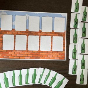 May include: A brick wall game with ten green glass bottle cards numbered 1 to 10. The cards are laid out in a vertical line on a wooden surface. The brick wall game has ten blank spaces for the cards to be placed.