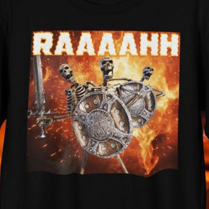 May include: Black t-shirt with a graphic of three skeleton warriors with shields and a sword, set against a fiery background. The word "RAAAHH" is displayed above the skeletons in a bold, illuminated font. A fantasy-themed apparel item.