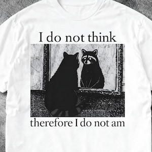 May include: White t-shirt featuring a black and white graphic of a raccoon looking in a mirror at itself. The text "I do not think" is above the image, and "therefore I do not am" is below.
