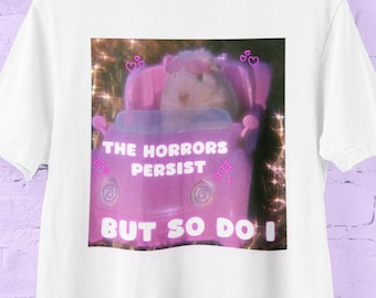 May include: White t-shirt with a pink graphic of a hamster in a pink car. The graphic has the text "The Horrors Persist But So Do I".