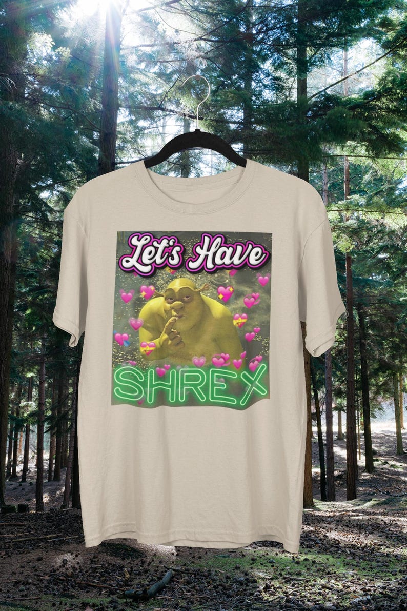 May include: A beige t-shirt with a green Shrek character image and the text "Let's Have Shrek" in pink and green neon lettering.