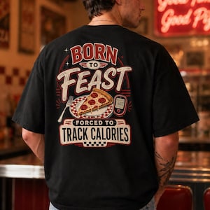 Könnte beinhalten: Ein schwarzes T-Shirt mit einem Grafikdruck auf der Rückseite und dem Text BORN TO FEAST FORCED TO TRACK CALORIES. Das Motiv zeigt ein Stück Peperoni-Pizza auf einem Teller, eine Gabel und ein digitales Blutzuckermessgerät mit der Anzeige 600.