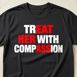 Könnte beinhalten: Ein schwarzes T-Shirt mit kurzen Ärmeln und dem Text "TREAT HER WITH COMPASSION" in einer fetten Blockschrift. Die Wörter "TREAT", "HER" und "ASS" sind in Rot gedruckt, während die restlichen Buchstaben in Weiß gehalten sind.