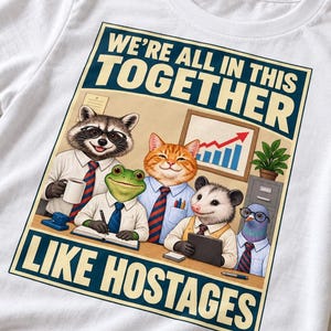 Könnte beinhalten: Ein weißes T-Shirt mit einer Grafik von einem Waschbären, Frosch, einer Katze, einem Opossum und einer Taube in Bürokleidung. Der Text lautet WE'RE ALL IN THIS TOGETHER LIKE HOSTAGES. Die Tiere sitzen an einem Schreibtisch mit einem Diagramm.