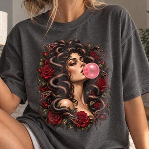 Może przedstawiać: Ciemnoszary t-shirt z krótkim rękawem z nadrukiem graficznym przedstawiającym postać z wężami zamiast włosów, wydmuchującą różową bańkę z gumy do żucia, otoczoną ciemnoczerwonymi różami i zielonymi liśćmi na przodzie ubrania.