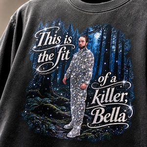 Op de afbeelding: Een antracietgrijs sweatshirt met een grafische print van een persoon in een sprankelende, glitterende outfit in een donkerblauw bos. De tekst luidt, This is the fit of a killer, Bella, in een wit cursief lettertype met sprankelende accenten.